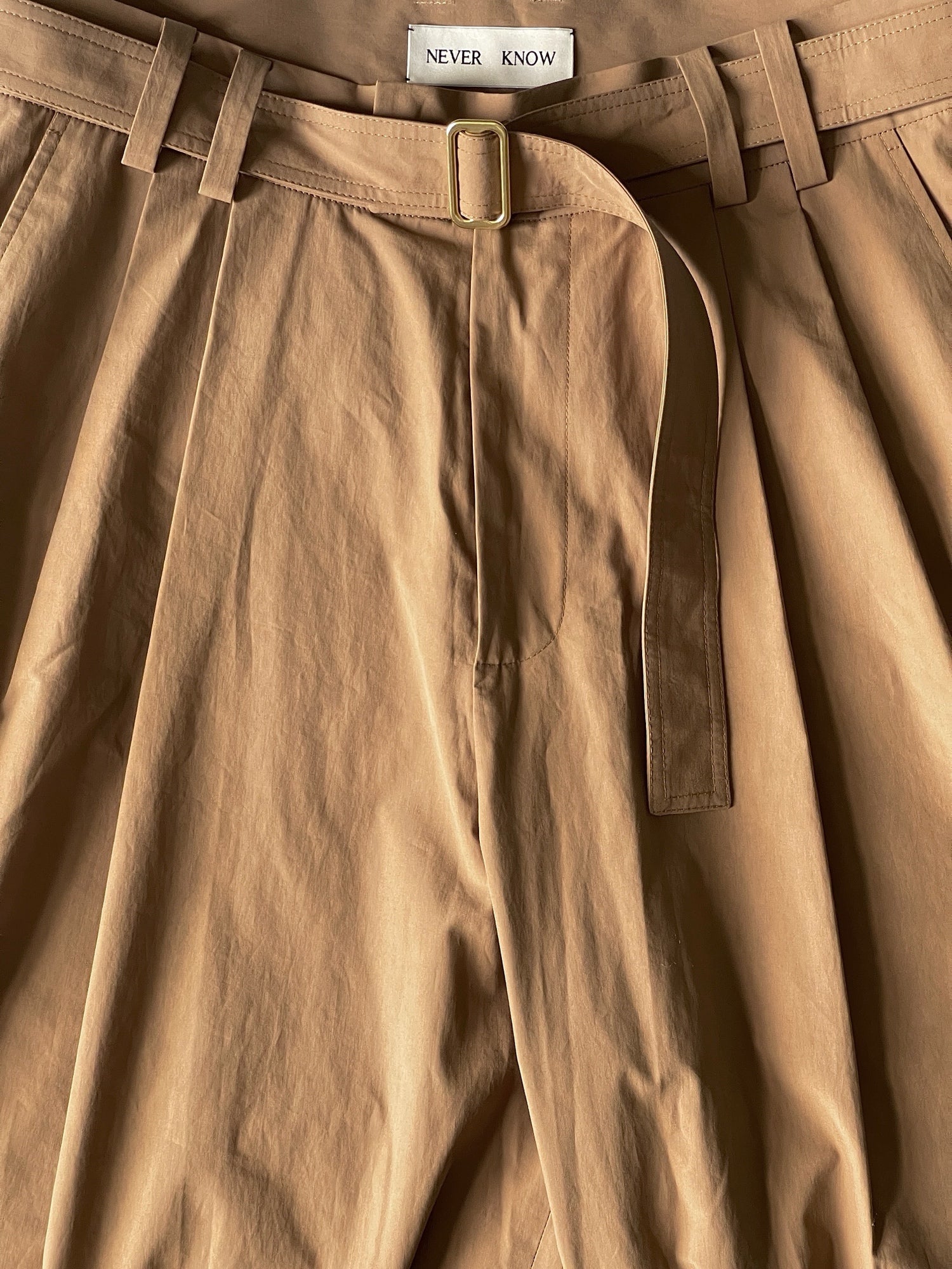 Close up of camel beige color pleated wide tailored trousers with belt.