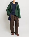 Person wearing a green jacket, navy shirt, brown pants, and brown shoes on a white background