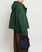 Person wearing a green jacket and brown pants holding a blue bag against a white background