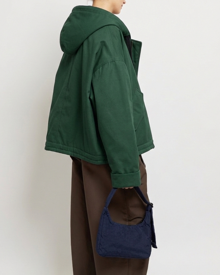 Person wearing a green jacket and brown pants holding a blue bag against a white background